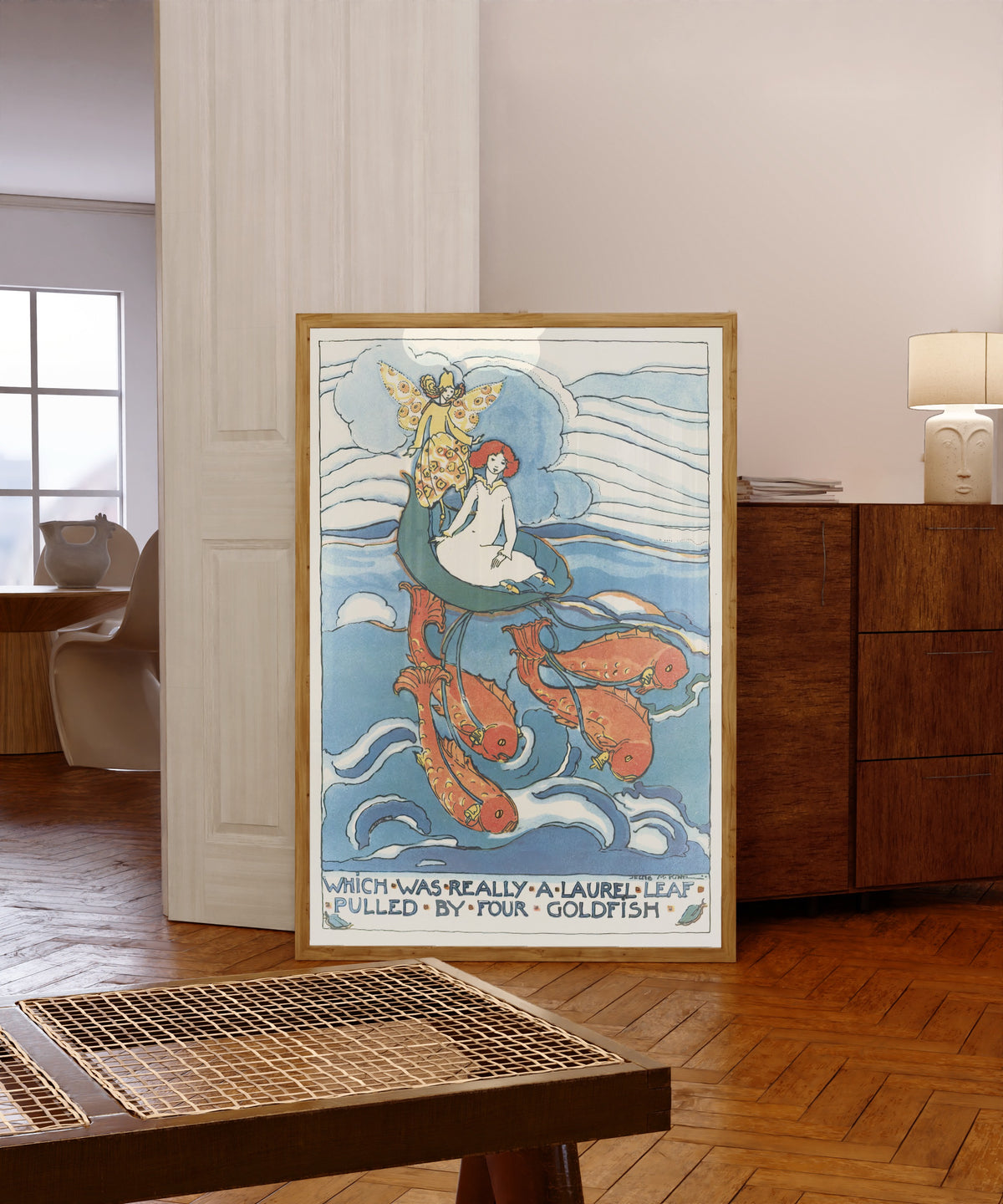 Framed art print of Mummy's Bedtime Story Book: Which Was Really a Laurel… by Jessie M. King, in a light wood frame leaning in a warm room with a parquet floor
