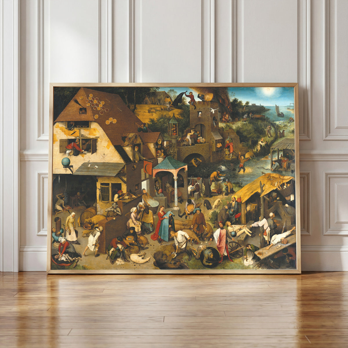 Framed art print of Netherlandish Proverbs by Pieter Bruegel the Elder, in a light wood frame leaning against a panelled white wall