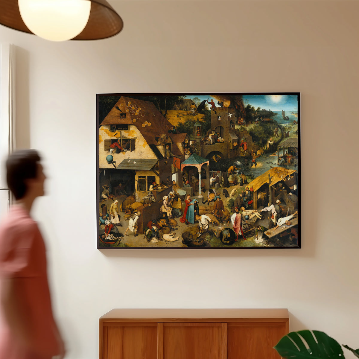 Framed art print of Netherlandish Proverbs by Pieter Bruegel the Elder, in a slim black frame on a warm wall in a sunlit room