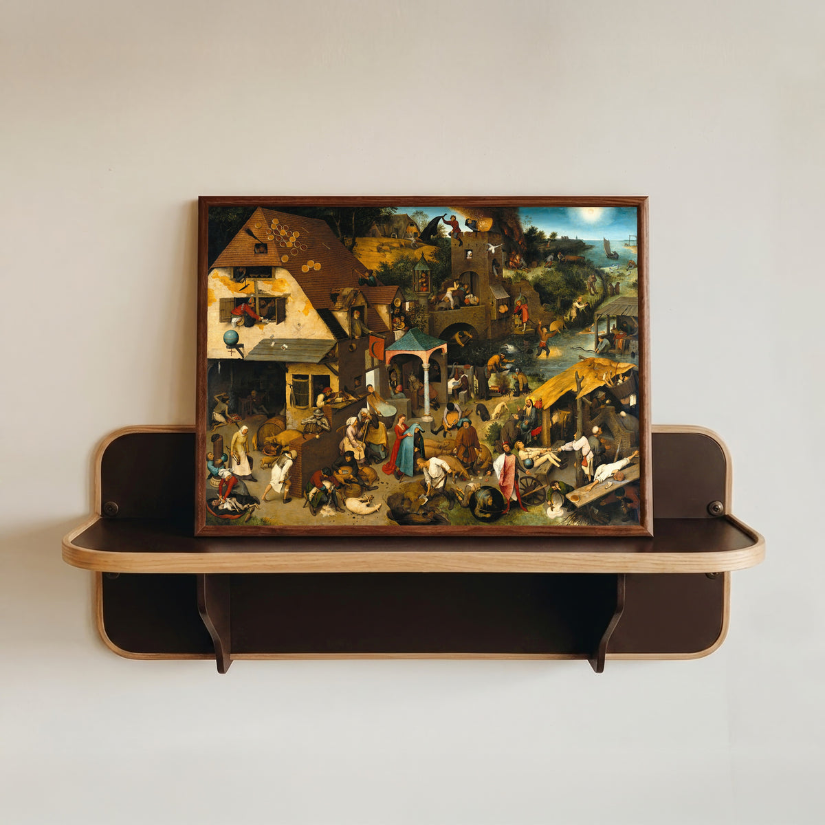 Framed art print of Netherlandish Proverbs by Pieter Bruegel the Elder, in a dark wood frame resting on a wall shelf