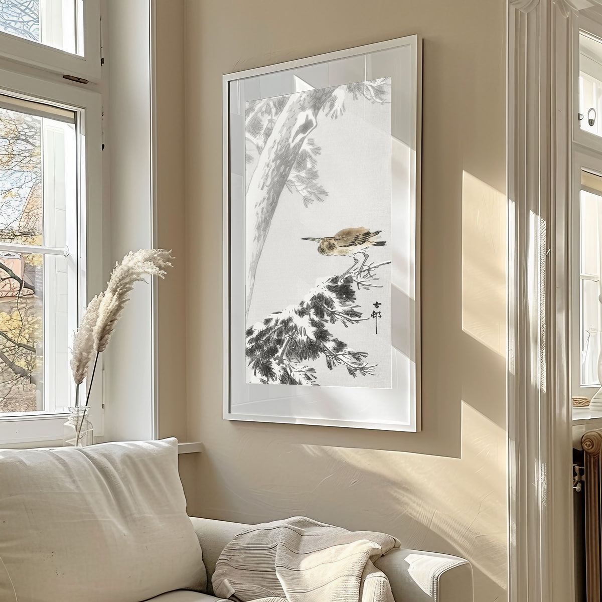 Framed art print of Night Heron on a Snowy Pine Branch by Ohara Koson, in a sunlit living room above a sofa