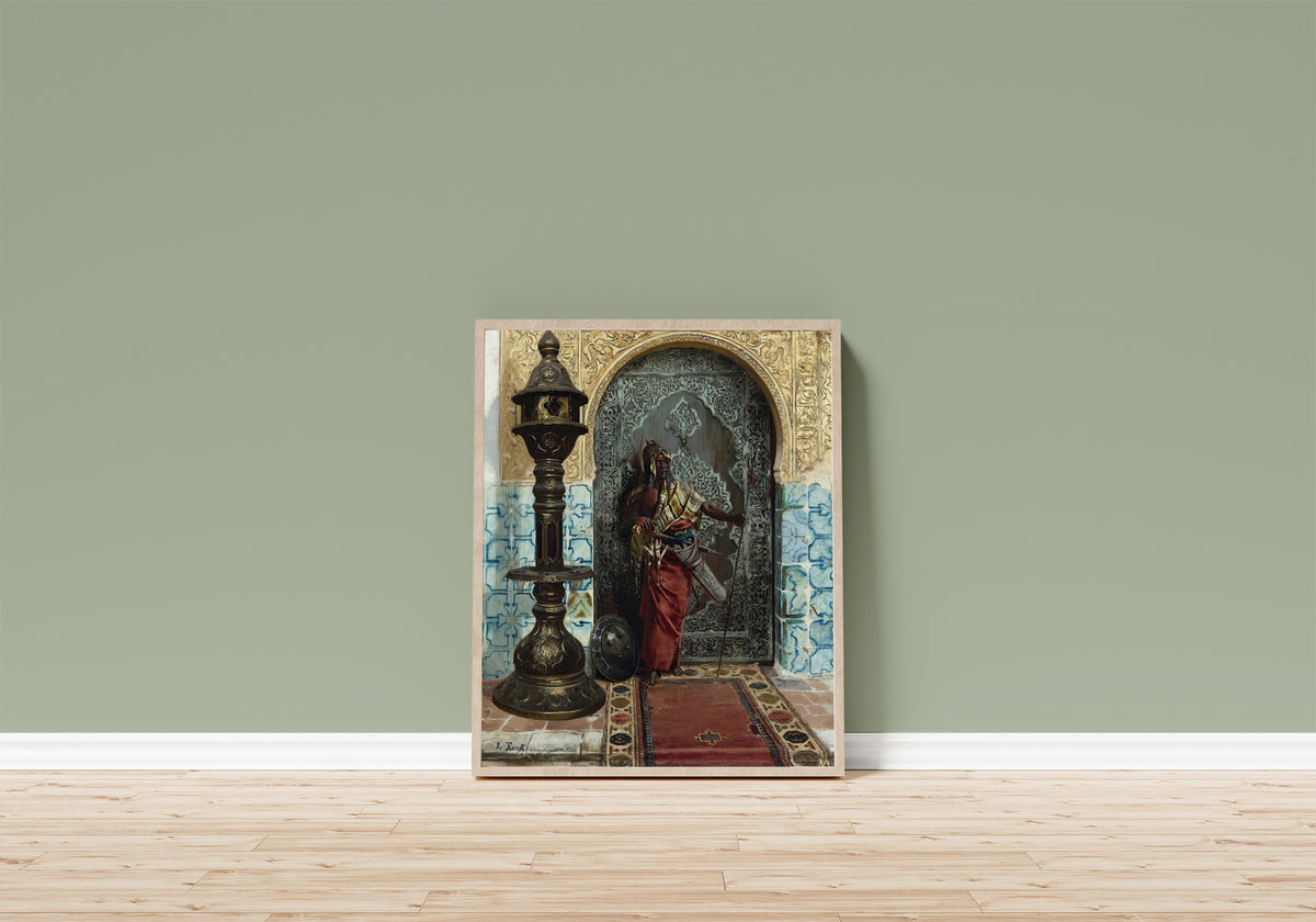 Framed art print of Nubian Guard by Rudolf Ernst, in a light wood frame leaning on a sage green wall above a wooden floor