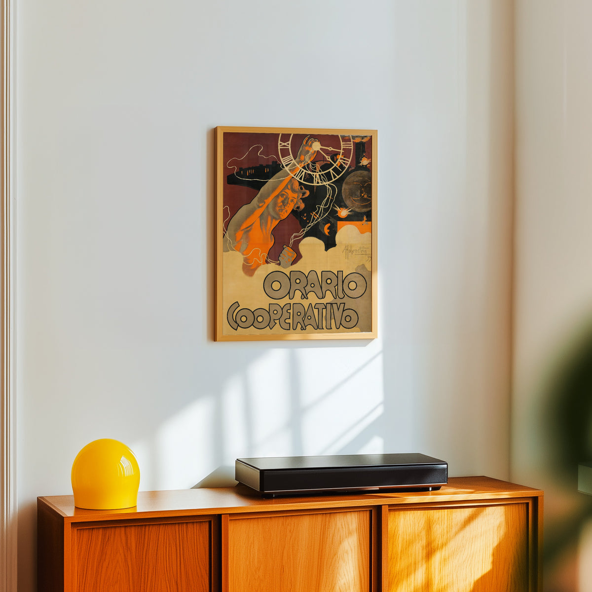 Framed art print of Orario Cooperativo by Adolfo Hohenstein, in a light wood frame on a white wall above an orange sideboard