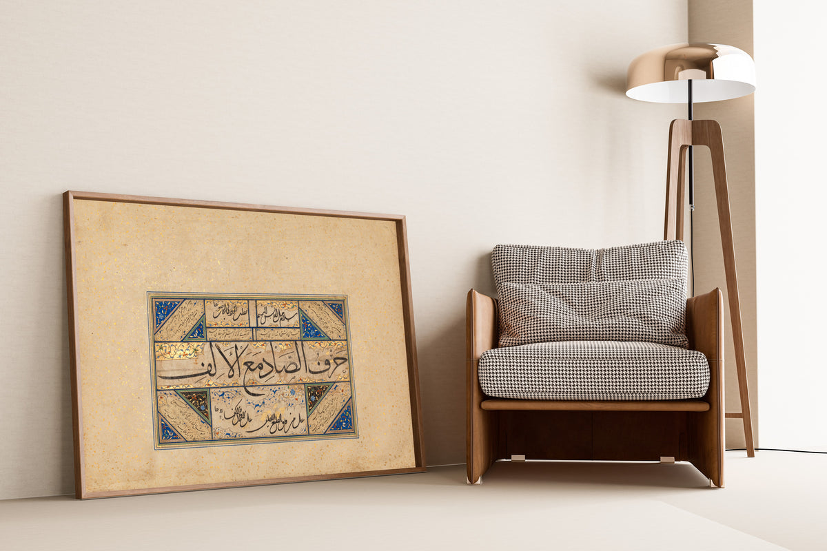 Framed art print of Page of Calligraphy by Sultan Muhammad Nur, leaning against a wall beside an armchair and a floor lamp