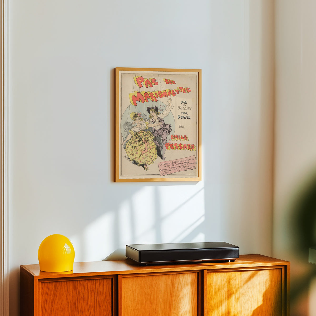 Framed art print of Pas des marionnettes, air de ballet pour piano par… by Théophile Steinlen, in a light wood frame on a white wall above an orange sideboard