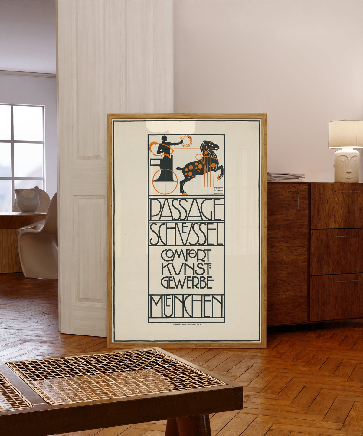 Framed art print of Passage Schüssel: Comfort Kunstgewerbe, München by Ludwig Hohlwein, in a light wood frame leaning in a warm room with a parquet floor