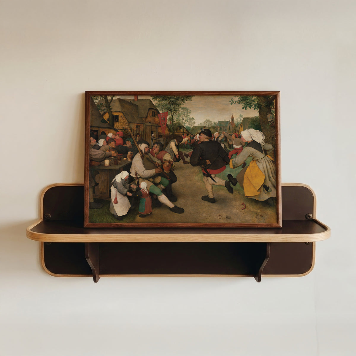 Framed art print of Peasant Dance by Pieter Bruegel the Elder, in a dark wood frame resting on a wall shelf