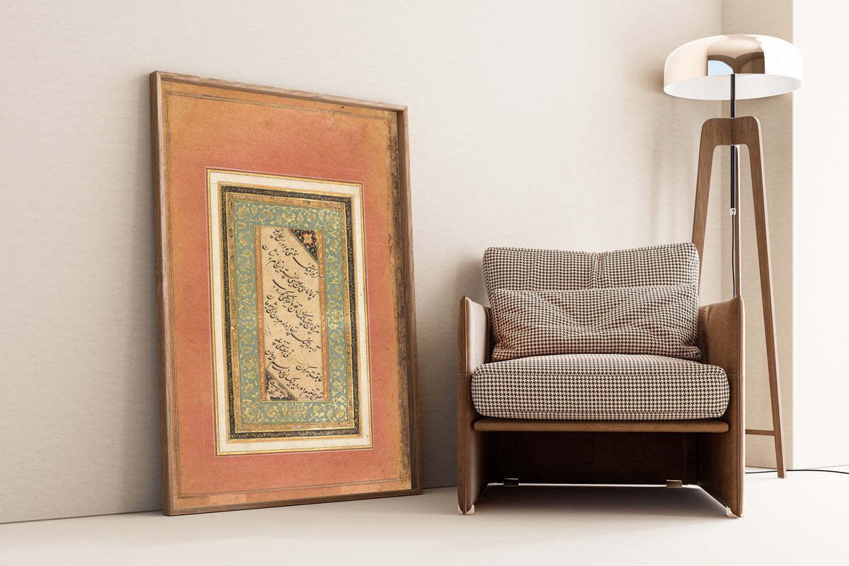 Framed art print of Persian Verses (Green and Gold Floral Border) by Sultan 'Ali al-Mashhadi, leaning against a wall beside an armchair and a floor lamp