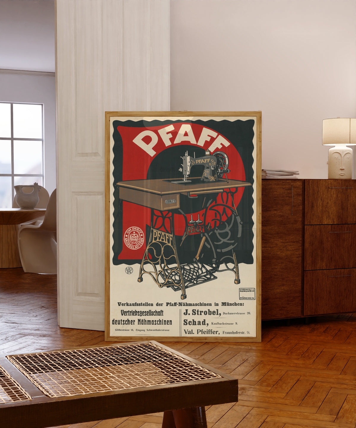 Framed art print of Pfaff: Vertriebsgesellschaft deutscher Nähmaschinen… by Ludwig Hohlwein, in a light wood frame leaning in a warm room with a parquet floor
