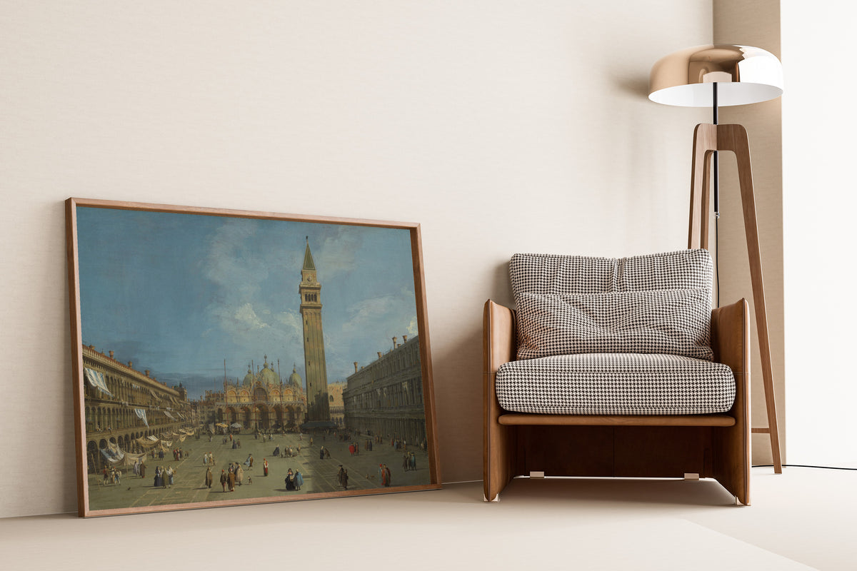 Framed art print of Piazza San Marco by Canaletto, leaning against a wall beside an armchair and a floor lamp