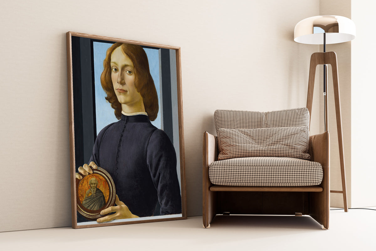 Framed art print of Portrait of a young man holding a roundel by Sandro Botticelli, leaning against a wall beside an armchair and a floor lamp
