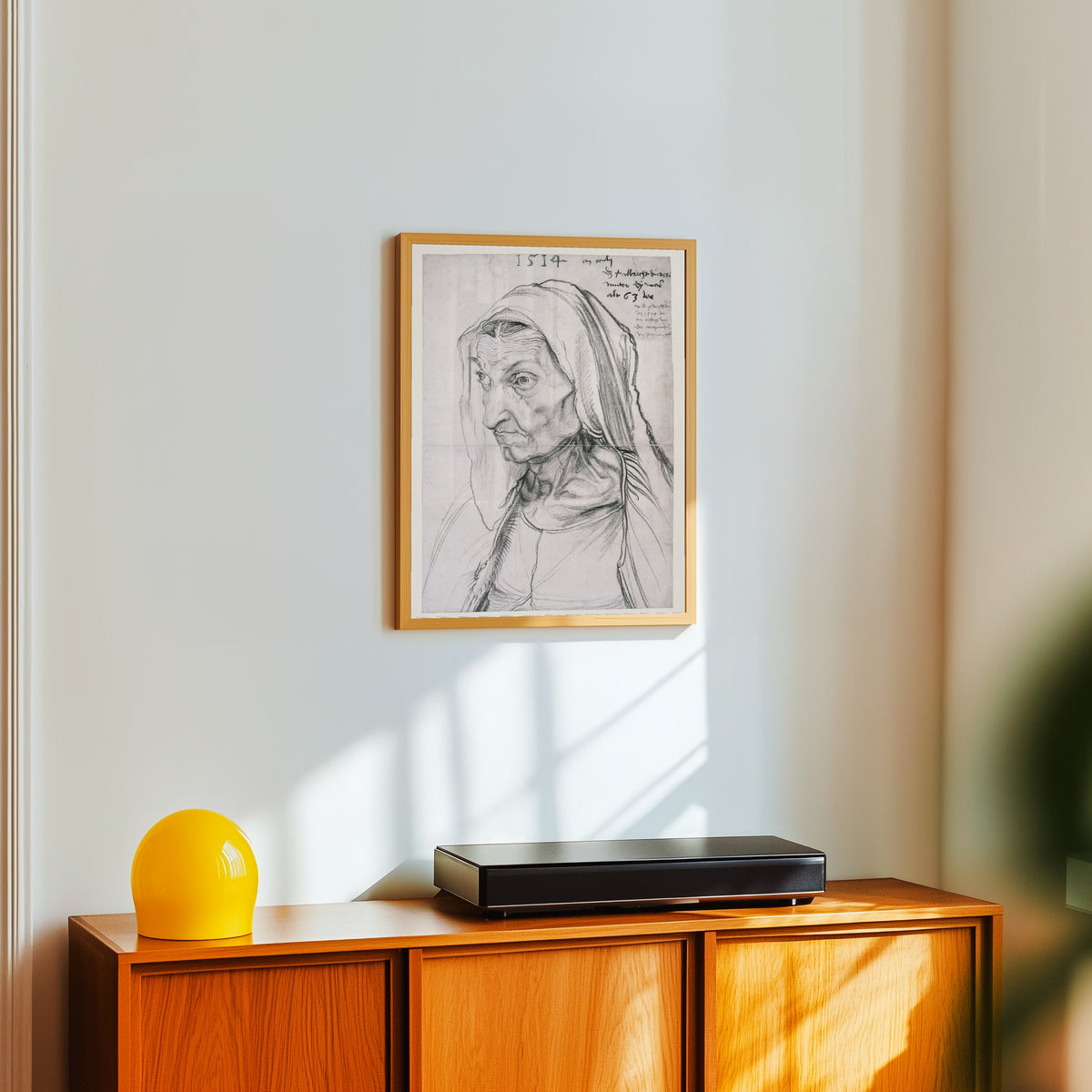 Framed art print of Portrait of the Artist's Mother at the Age of 63 by Albrecht Dürer, in a light wood frame on a white wall above an orange sideboard