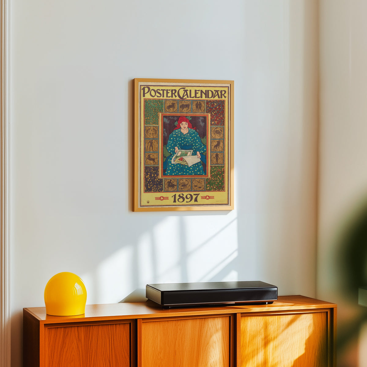 Framed art print of Poster Calendar, 1897 by Louis Rhead, in a light wood frame on a white wall above an orange sideboard