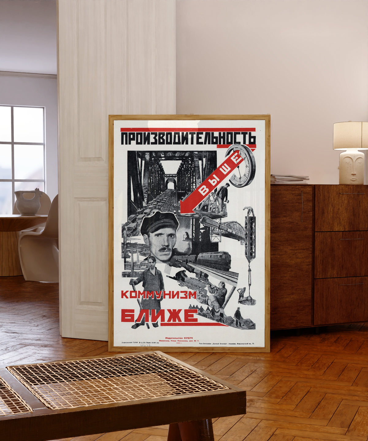 Framed art print of Productivity higher, communism closer, in a light wood frame leaning in a warm room with a parquet floor