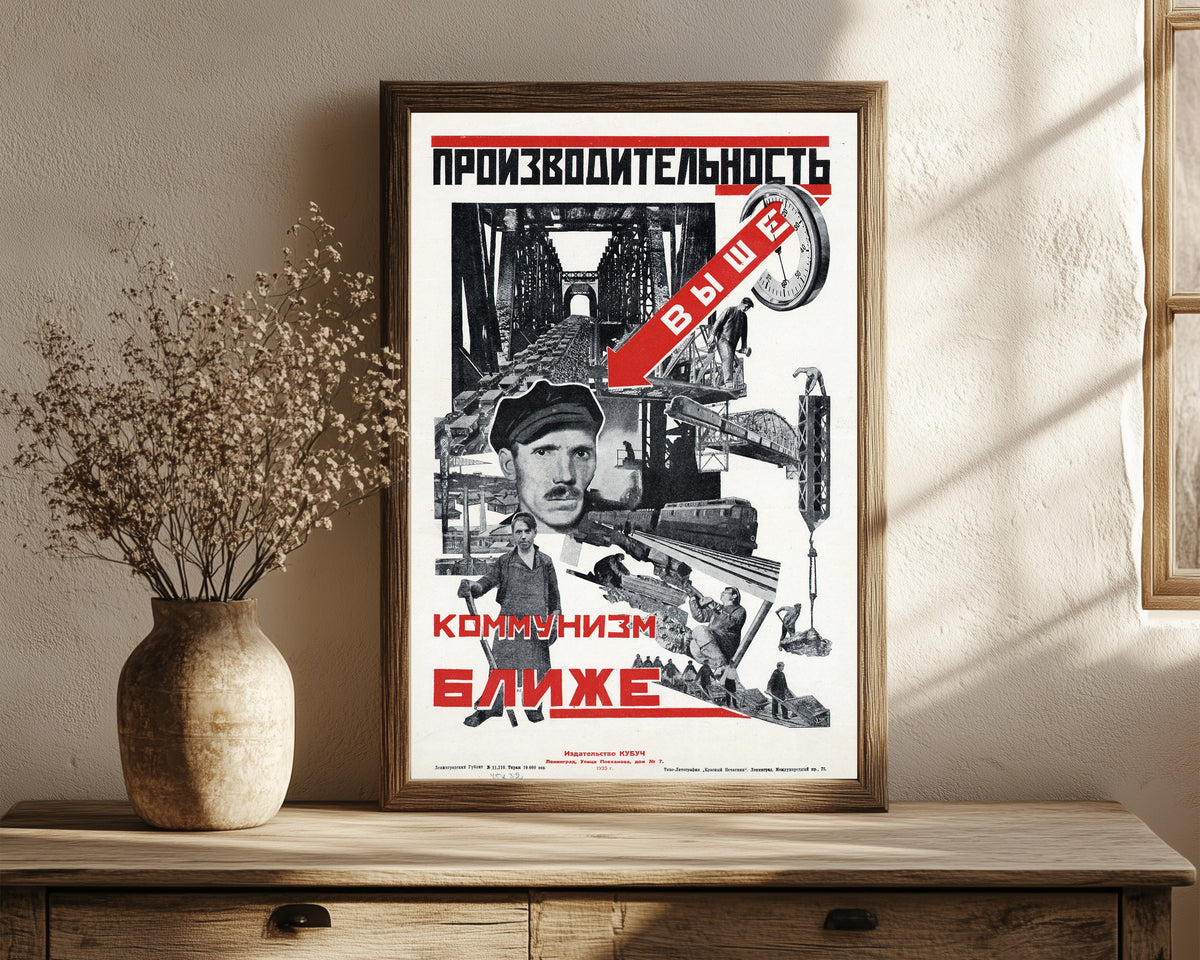 Framed art print of Productivity higher, communism closer, in a dark wood frame leaning on a rustic console beside dried flowers