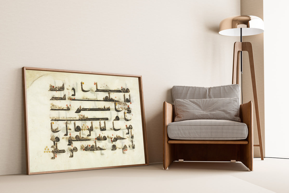 Framed art print of Qur'an Folio: Sura al-Saad, leaning against a wall beside an armchair and a floor lamp