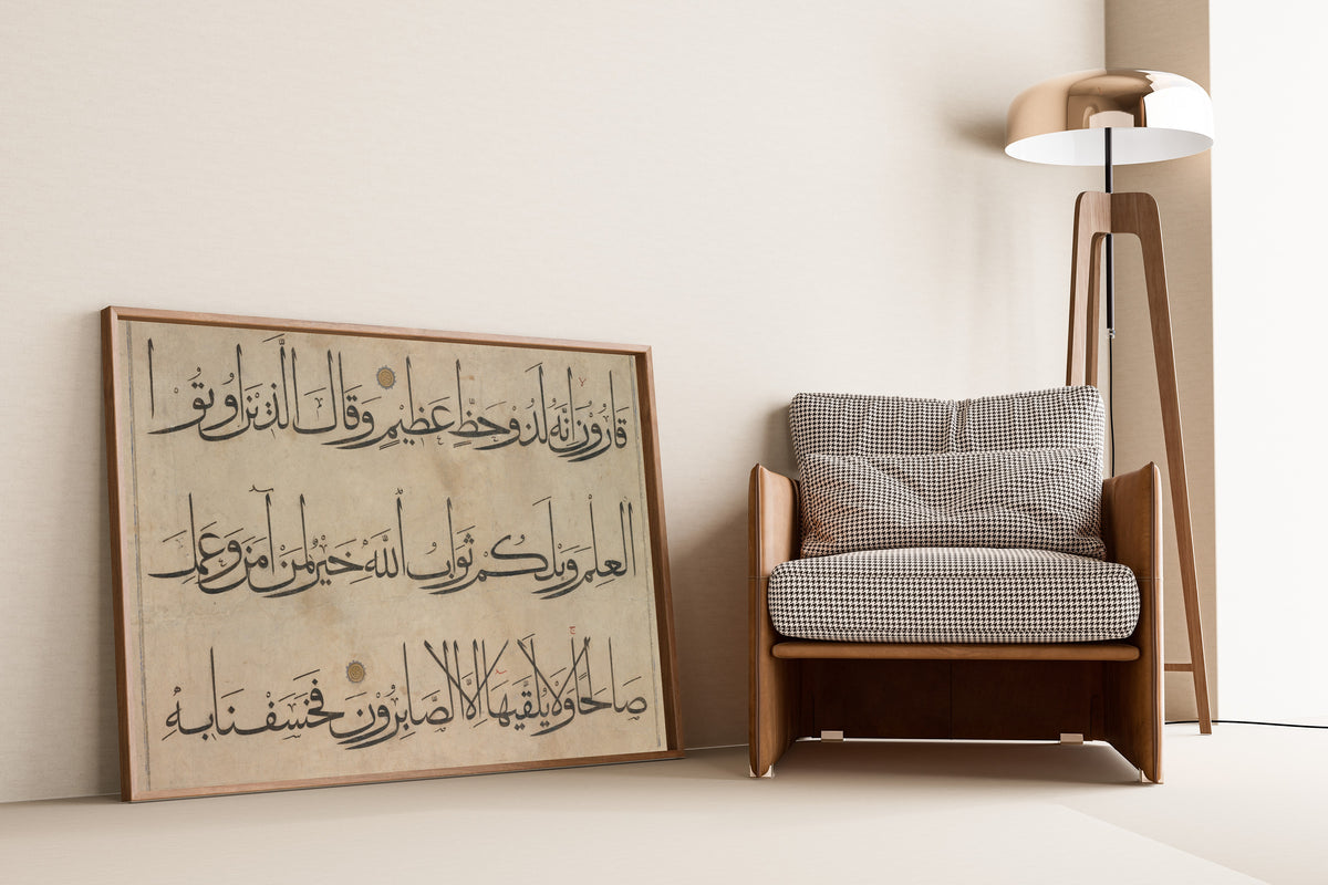 Framed art print of Qur'an Section (Three Lines) by `Umar Aqta', leaning against a wall beside an armchair and a floor lamp
