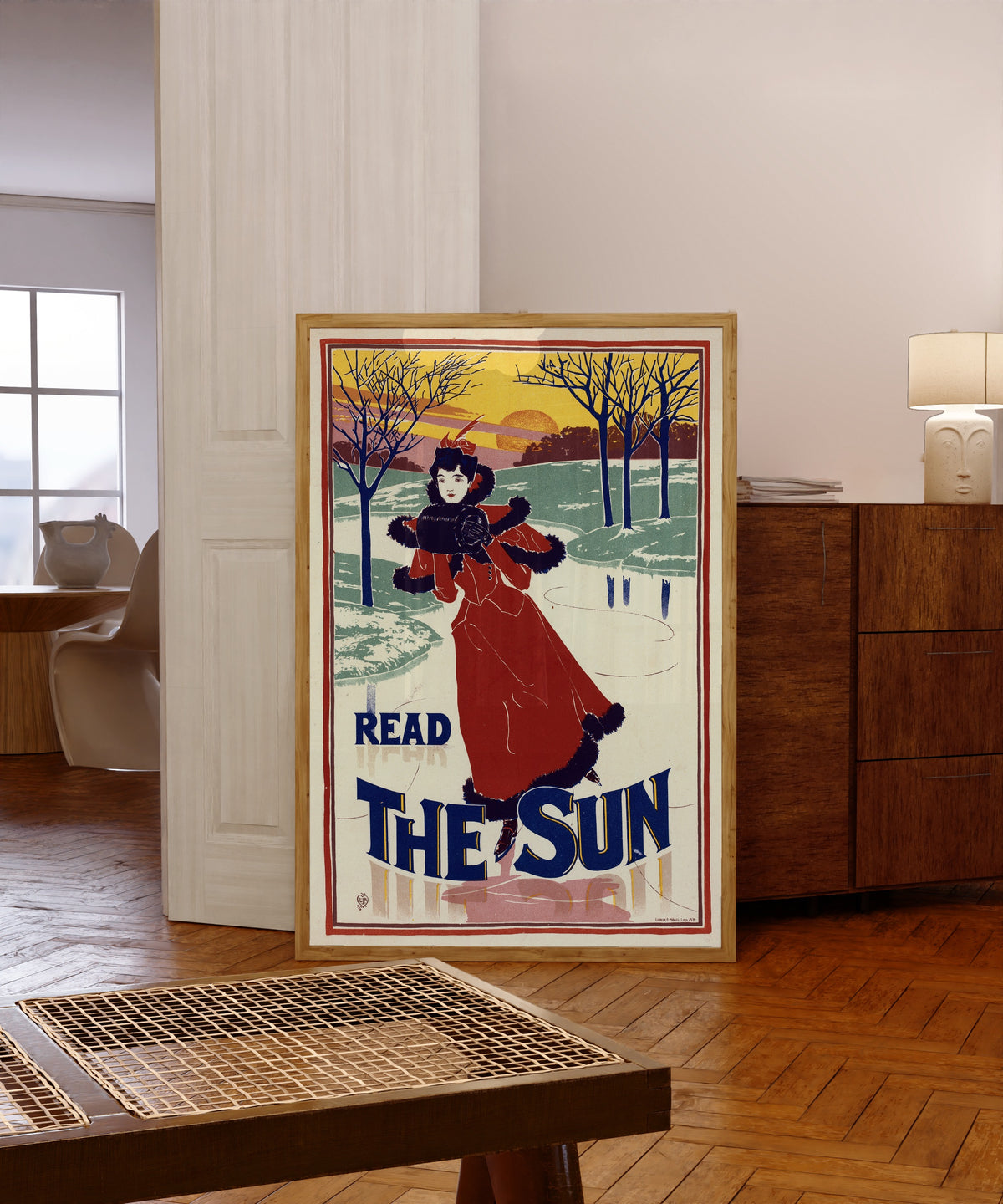 Framed art print of Read The Sun by Louis Rhead, in a light wood frame leaning in a warm room with a parquet floor