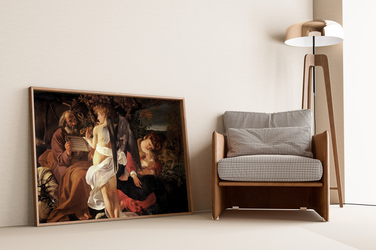 Framed art print of Rest on the Flight into Egypt by Caravaggio, leaning against a wall beside an armchair and a floor lamp