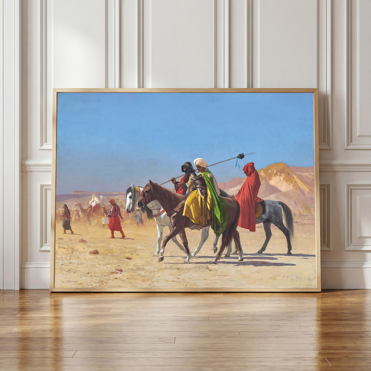 Framed art print of Riders Crossing the Desert by Jean-Léon Gérôme, in a light wood frame leaning against a panelled white wall