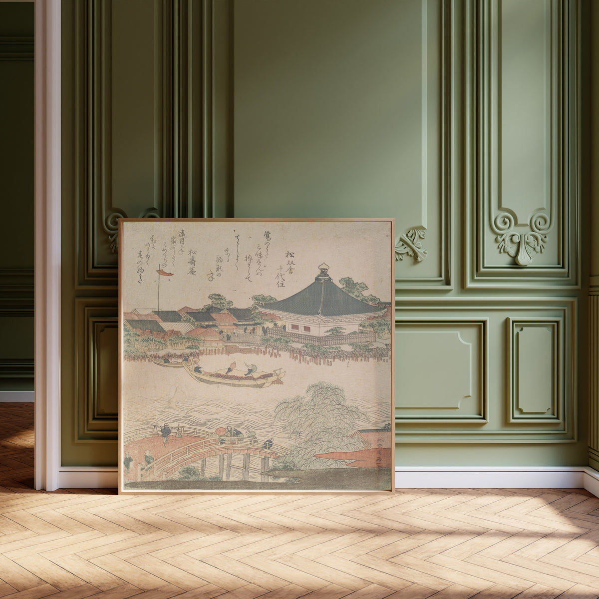 Framed art print of River Scene with Bridge in Foreground by Katsushika Hokusai, leaning against olive-green panelling on a herringbone floor
