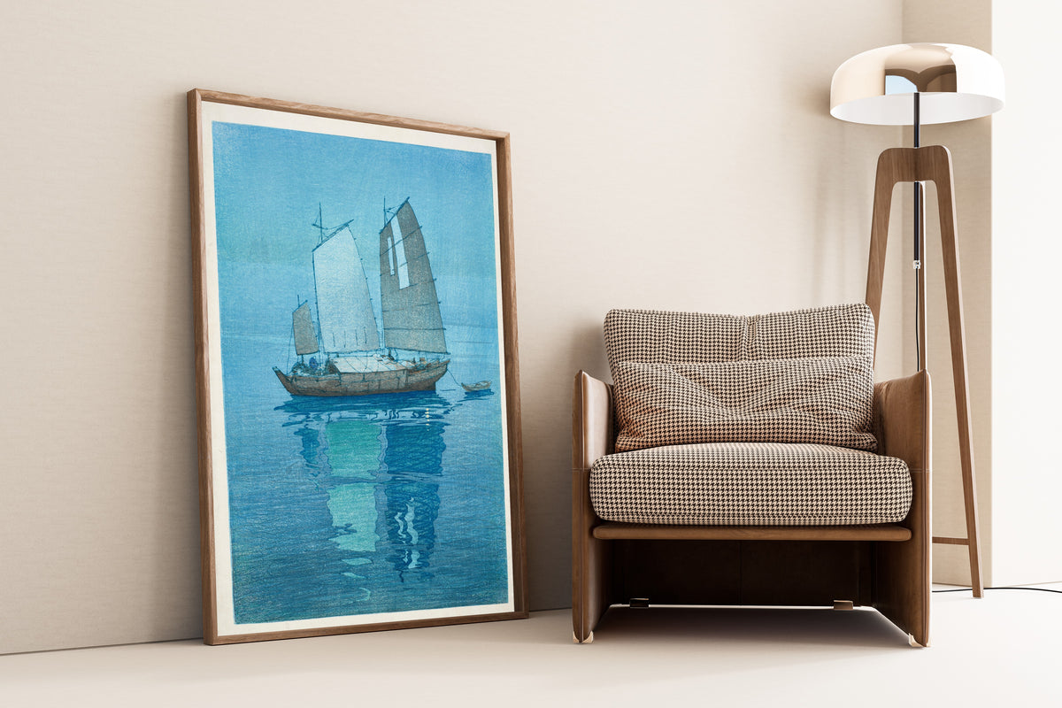 Framed art print of Sailing Boats by Hiroshi Yoshida, leaning against a wall beside an armchair and a floor lamp