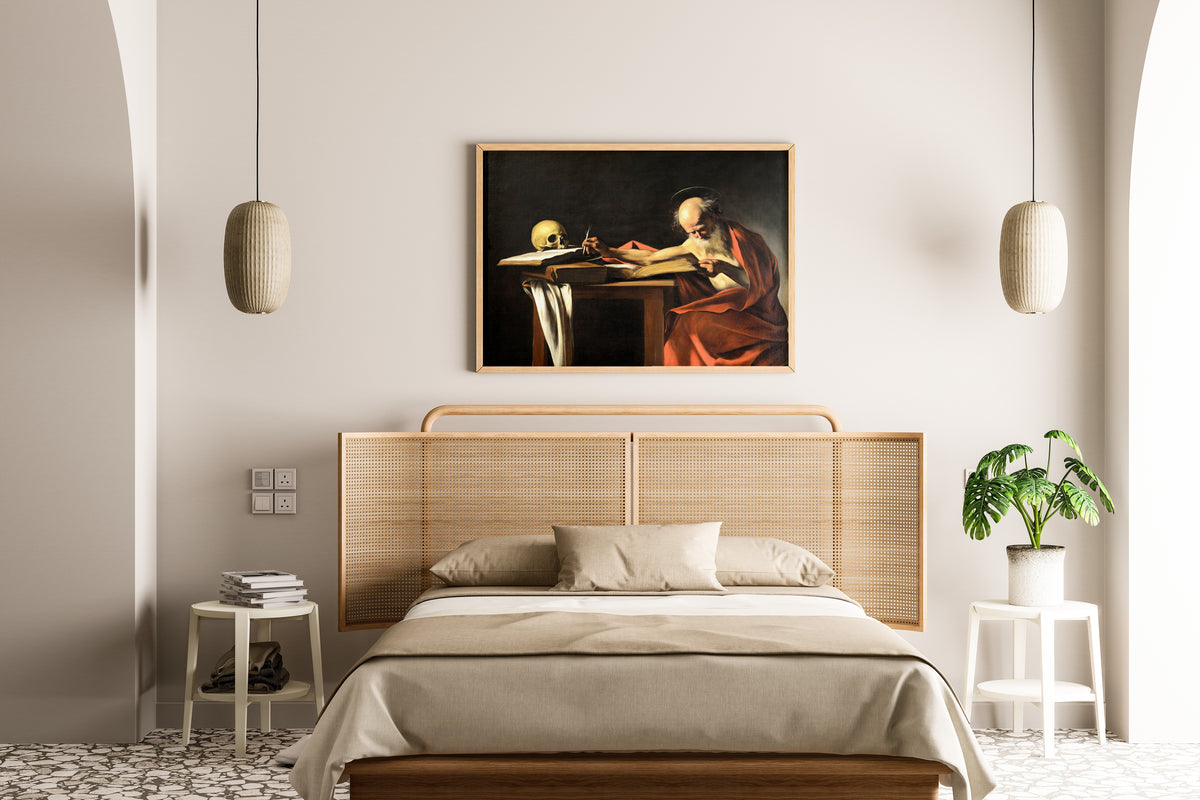 Framed art print of Saint Jerome Writing by Caravaggio, above a cane-headboard bed