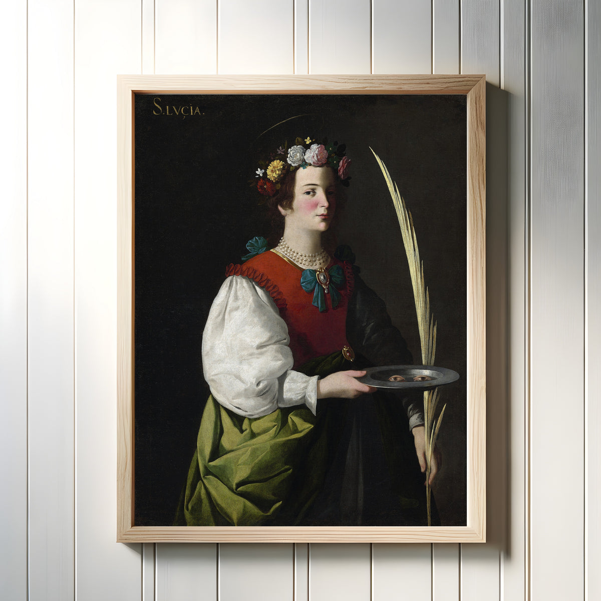 Framed art print of Saint Lucy by Francisco de Zurbarán, in a light wood frame on a white panelled wall
