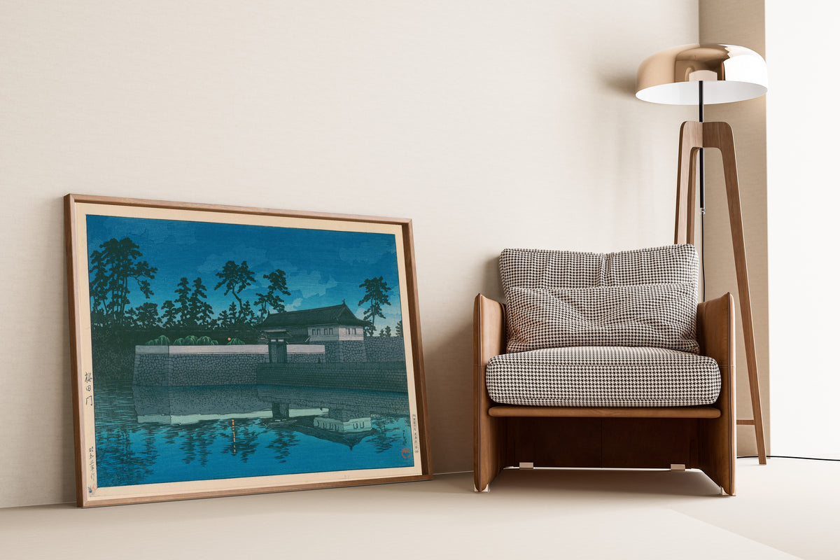 Framed art print of Sakurada Gate by Kawase Hasui, leaning against a wall beside an armchair and a floor lamp