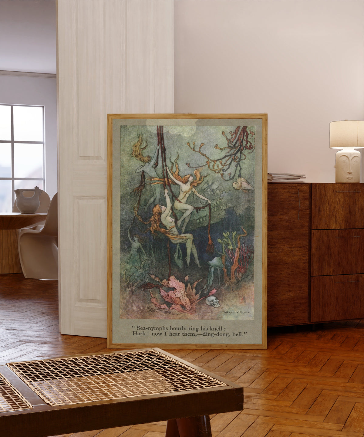 Framed art print of Sea-nymphs hourly ring his knell; Hark! now I hear… by Warwick Goble, in a light wood frame leaning in a warm room with a parquet floor