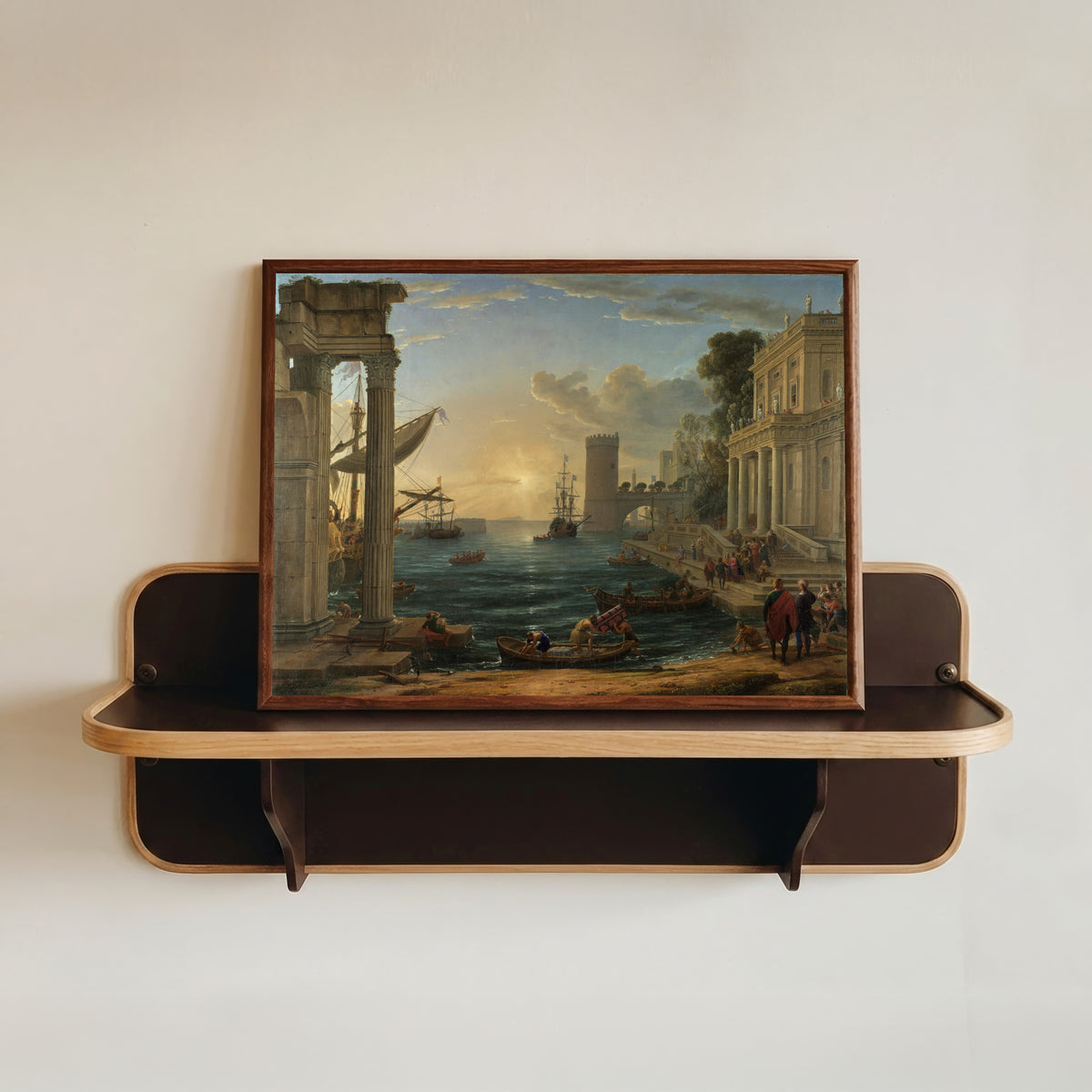 Framed art print of Seaport with the Embarkation of the Queen of Sheba by Claude Lorrain, in a dark wood frame resting on a wall shelf