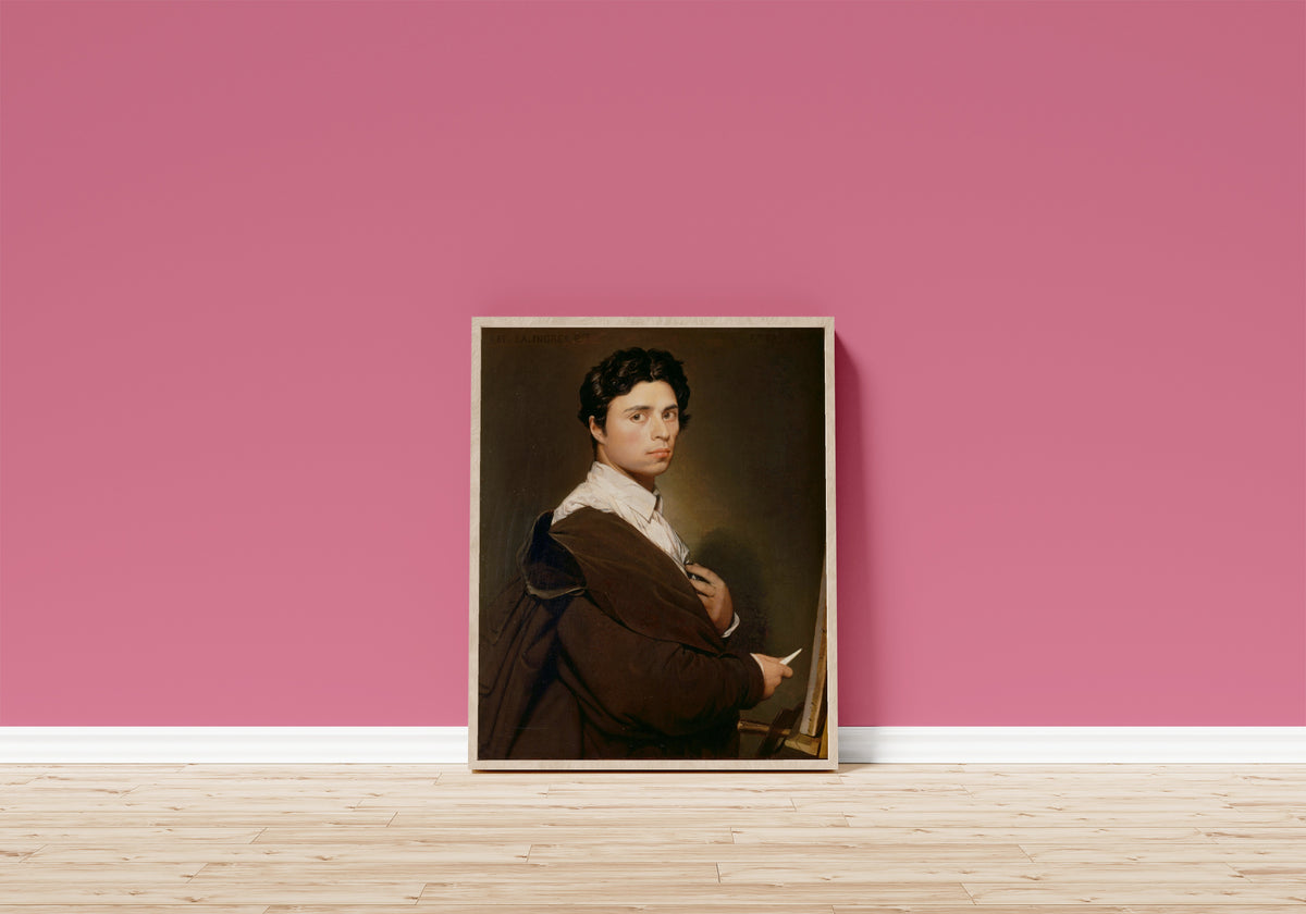 Framed art print of Self-Portrait Aged 24 by Jean-Auguste-Dominique Ingres, in a light wood frame leaning on a pink wall above a wooden floor