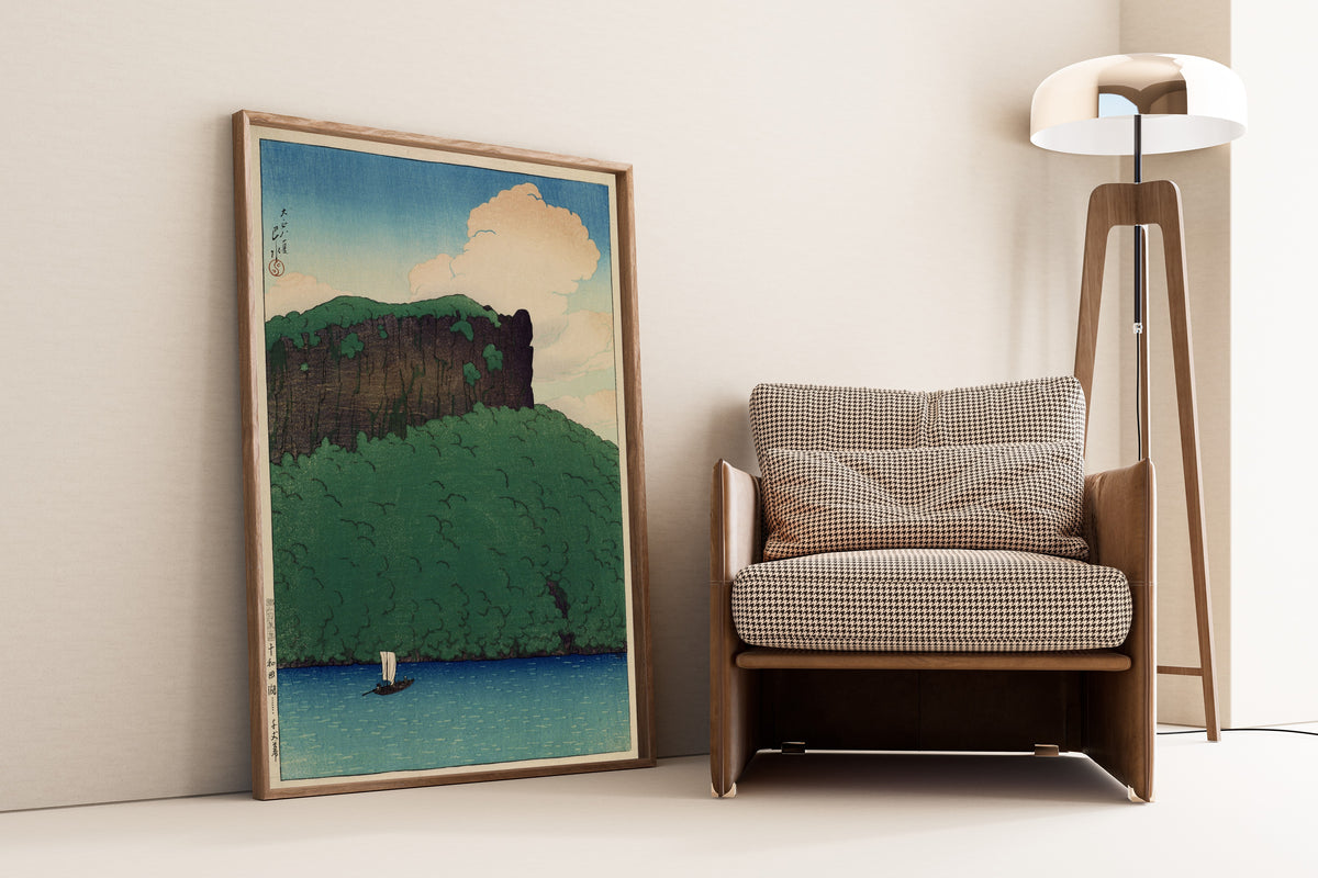 Framed art print of Senjo Cliff, Lake Towada by Kawase Hasui, leaning against a wall beside an armchair and a floor lamp