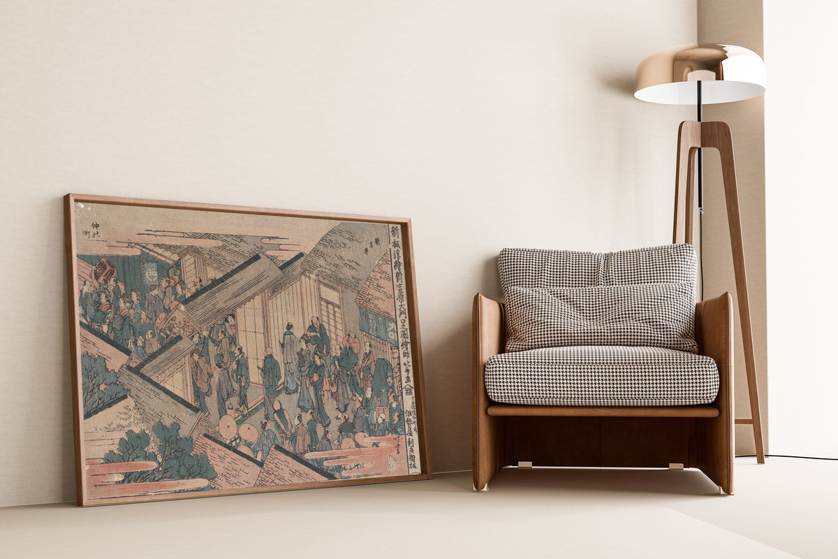 Framed art print of Shinpan ukie shin yoshiwara ōmonuchi no zu by Katsushika Hokusai, leaning against a wall beside an armchair and a floor lamp