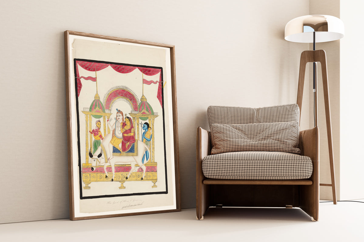 Framed art print of Shiva and Parvati on Nandi with Kartikeya and Ganesha by Kalighat painter, leaning against a wall beside an armchair and a floor lamp