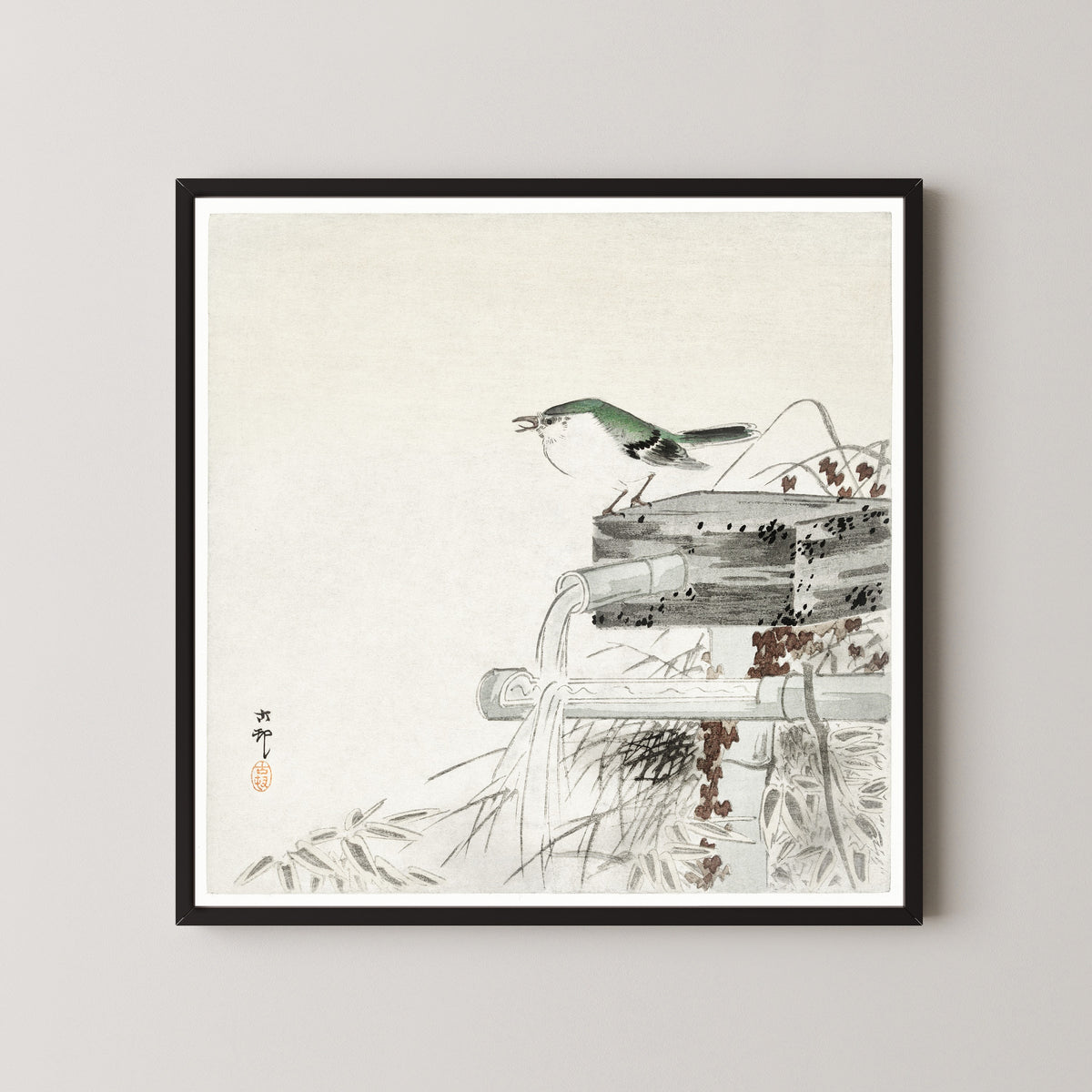 Framed art print of Siberian Blue Robin at a Bamboo Water Spout by Ohara Koson, in a black frame on a pale wall