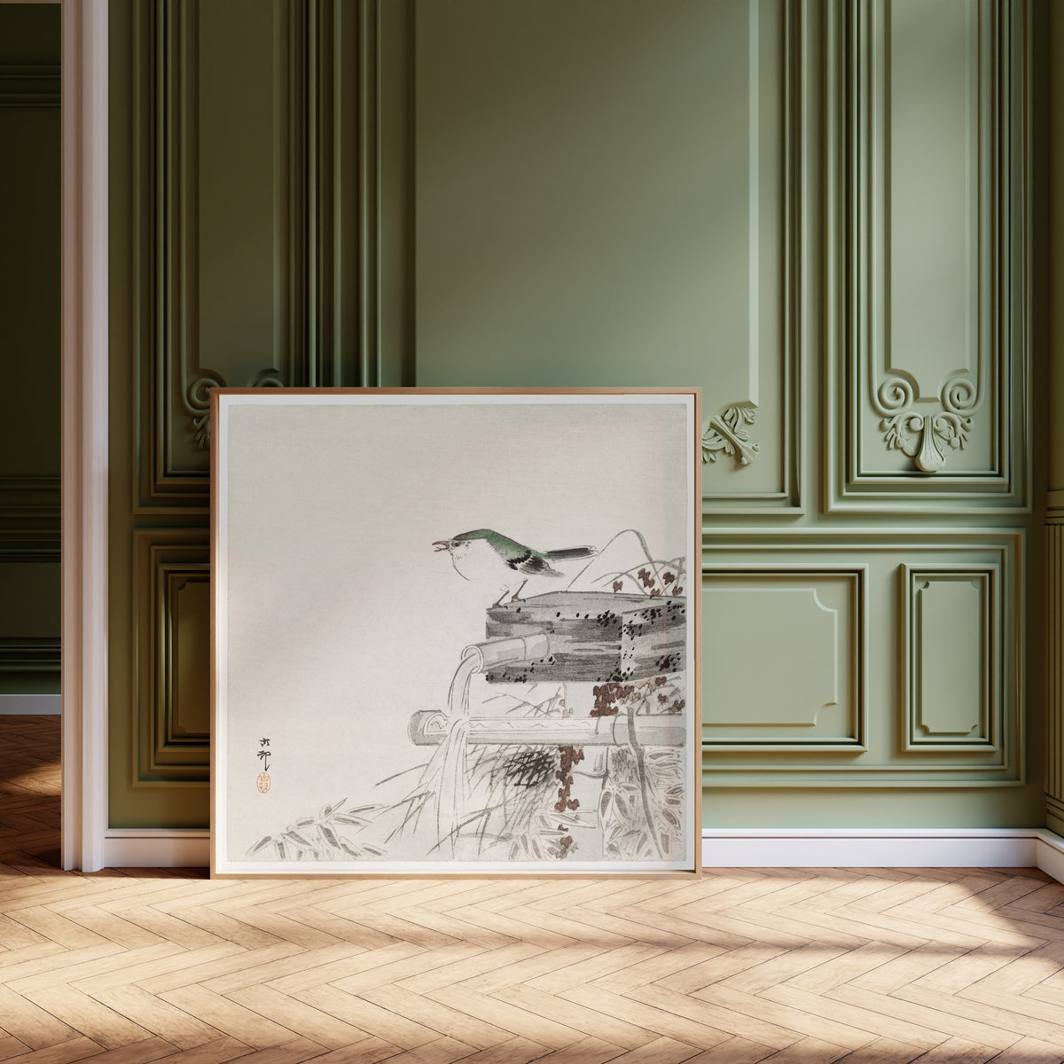 Framed art print of Siberian Blue Robin at a Bamboo Water Spout by Ohara Koson, leaning against olive-green panelling on a herringbone floor