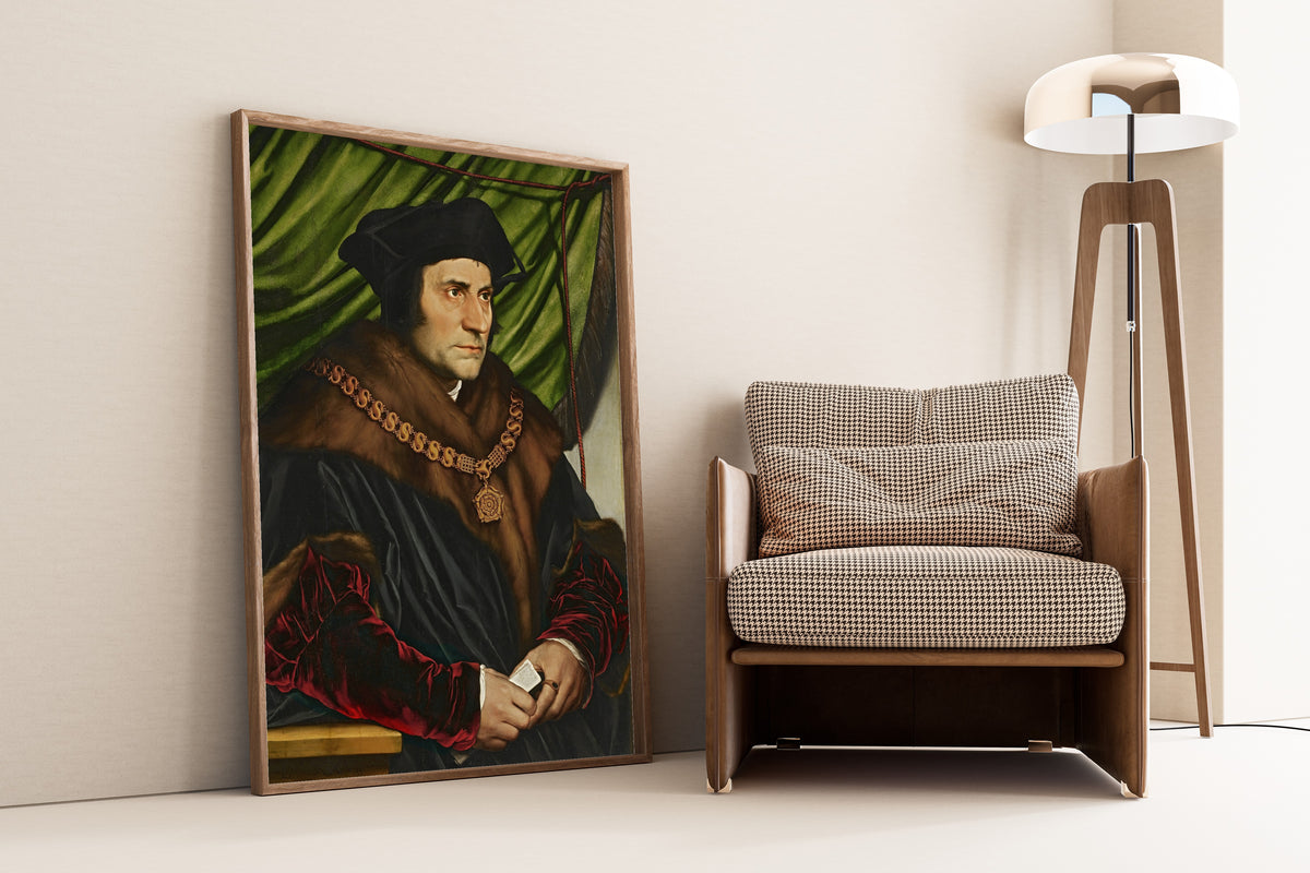 Framed art print of Sir Thomas More by Hans Holbein the Younger, leaning against a wall beside an armchair and a floor lamp