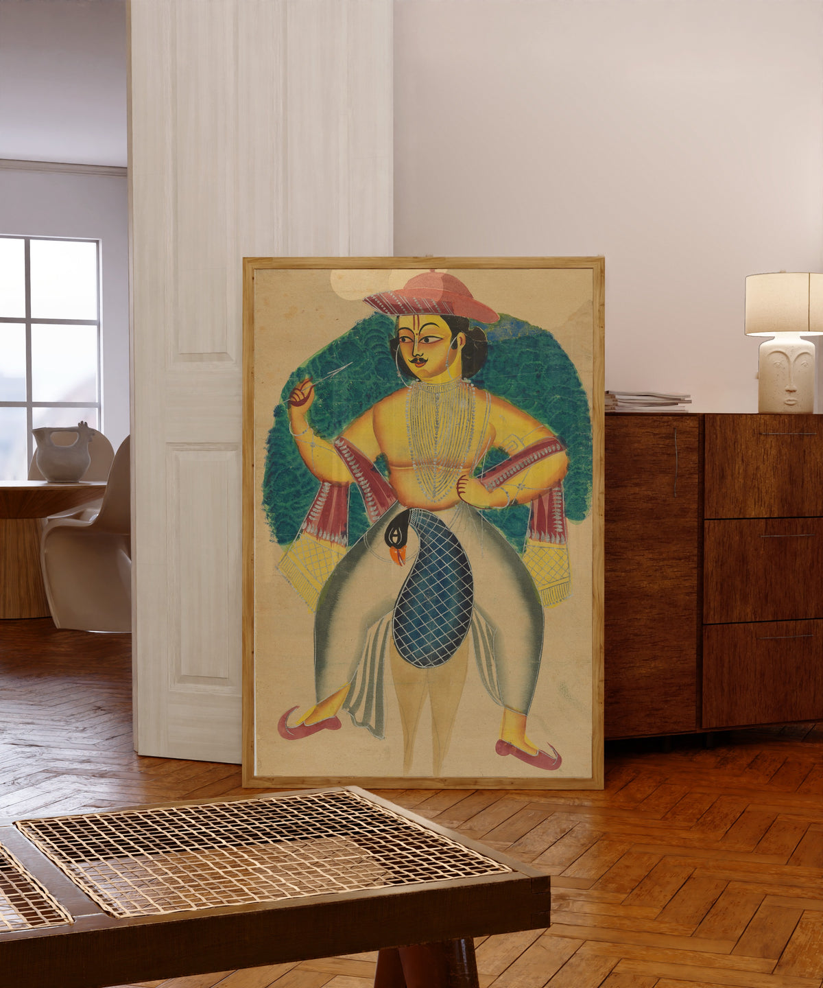Framed art print of Skanda on his peacock by Kalighat painter, in a light wood frame leaning in a warm room with a parquet floor