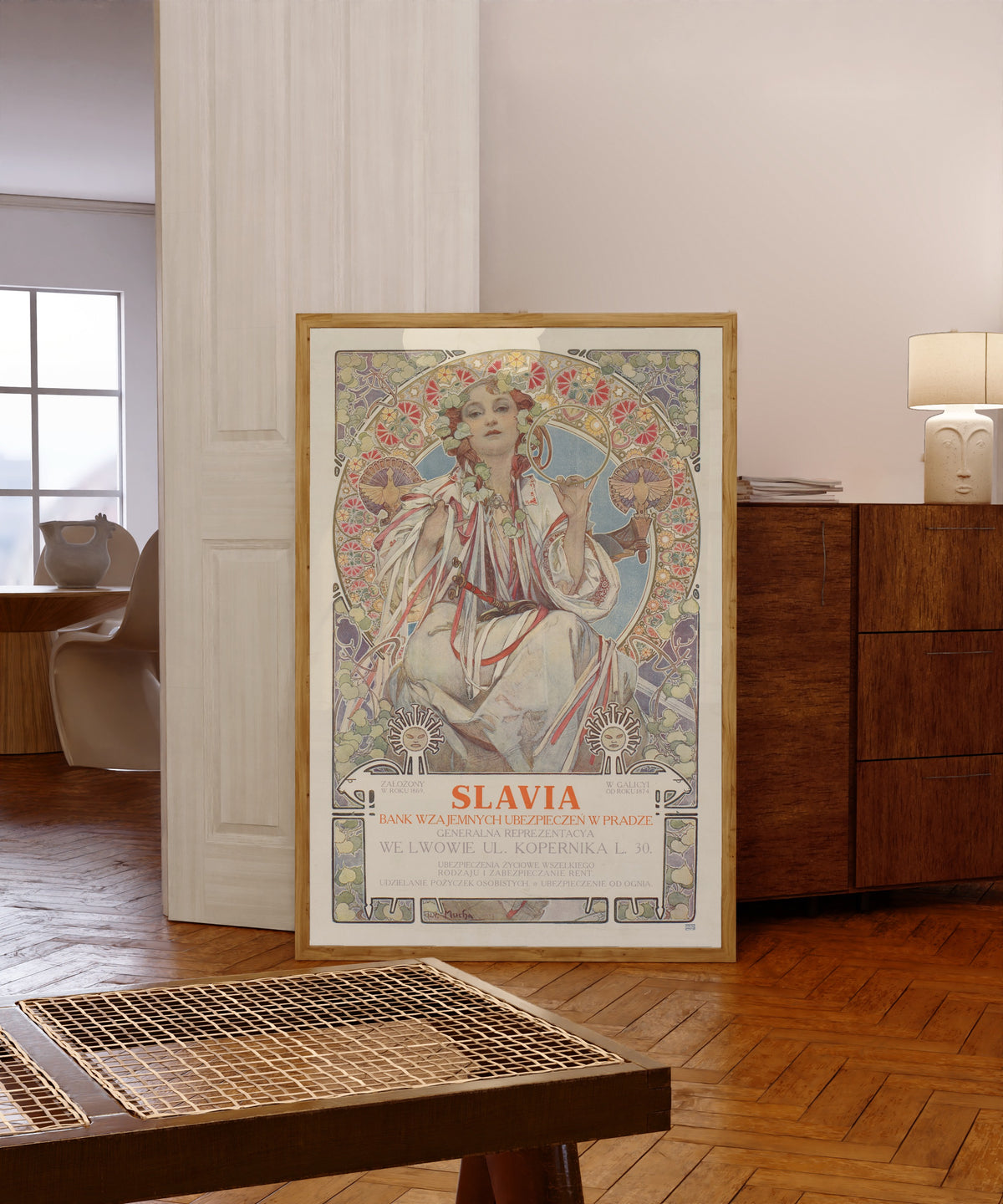 Framed art print of Slavia, Bank Wzajemnych Ubezpieczeń w Pradze by Alphonse Mucha, in a light wood frame leaning in a warm room with a parquet floor
