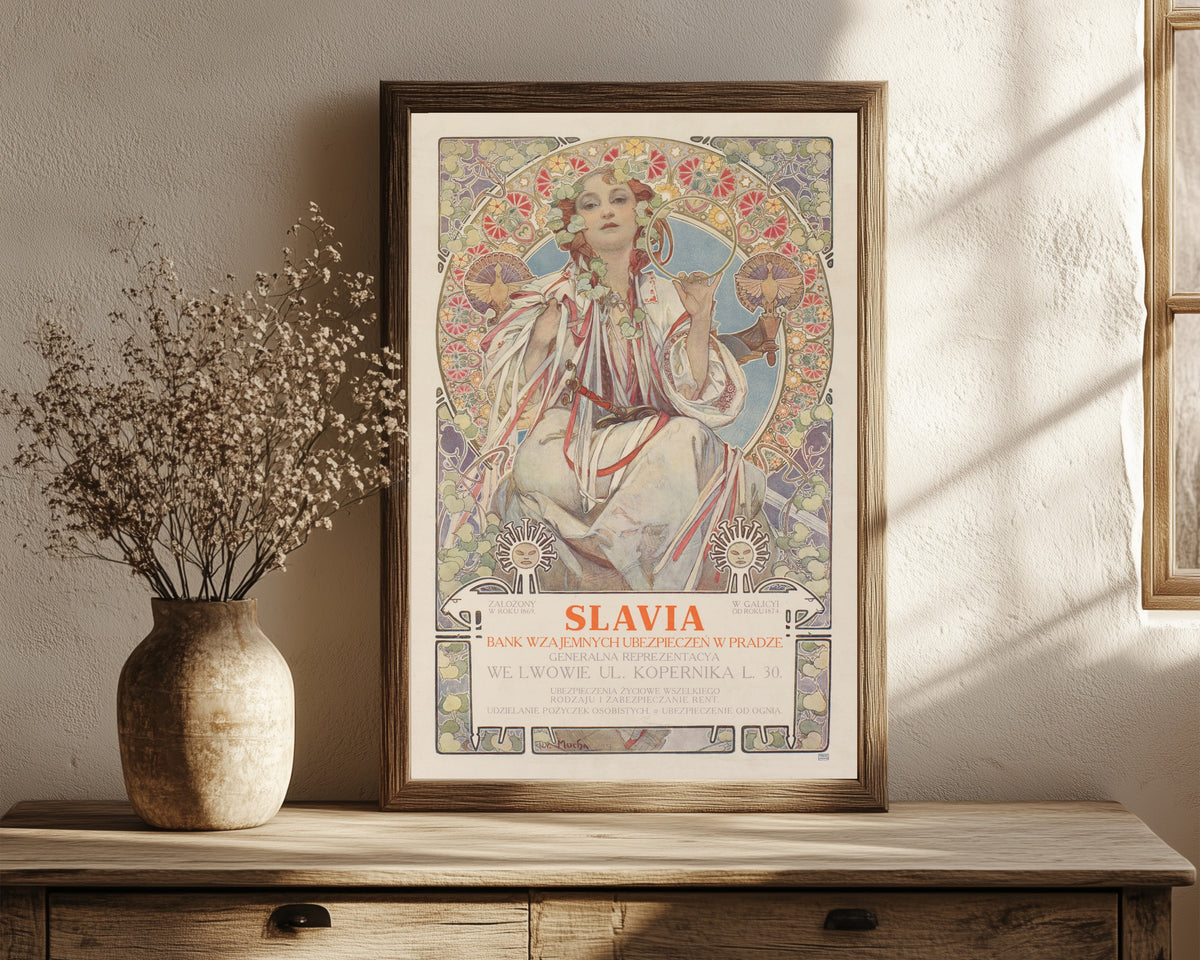 Framed art print of Slavia, Bank Wzajemnych Ubezpieczeń w Pradze by Alphonse Mucha, in a dark wood frame leaning on a rustic console beside dried flowers