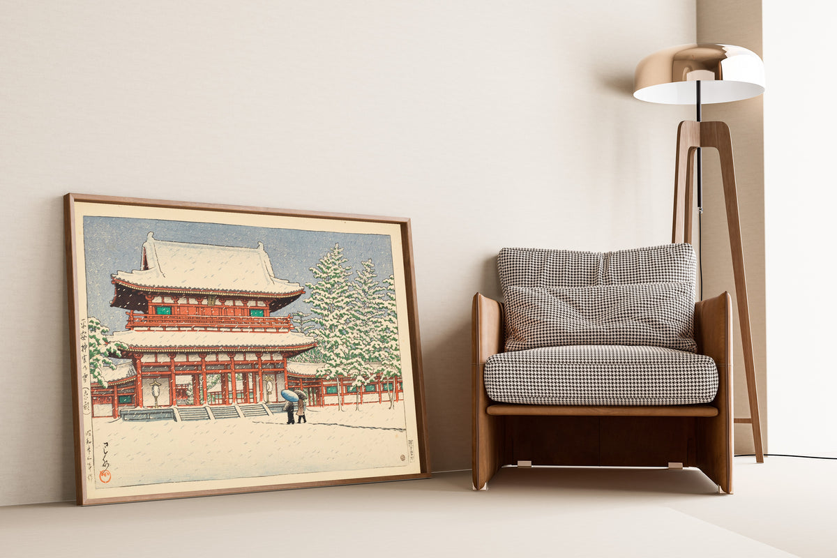 Framed art print of Snow at Heian Shrine, Kyoto by Kawase Hasui, leaning against a wall beside an armchair and a floor lamp