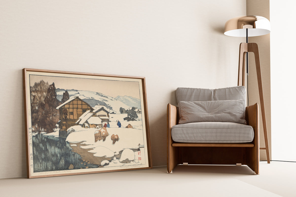 Framed art print of Snow at Kashiwabara by Hiroshi Yoshida, leaning against a wall beside an armchair and a floor lamp