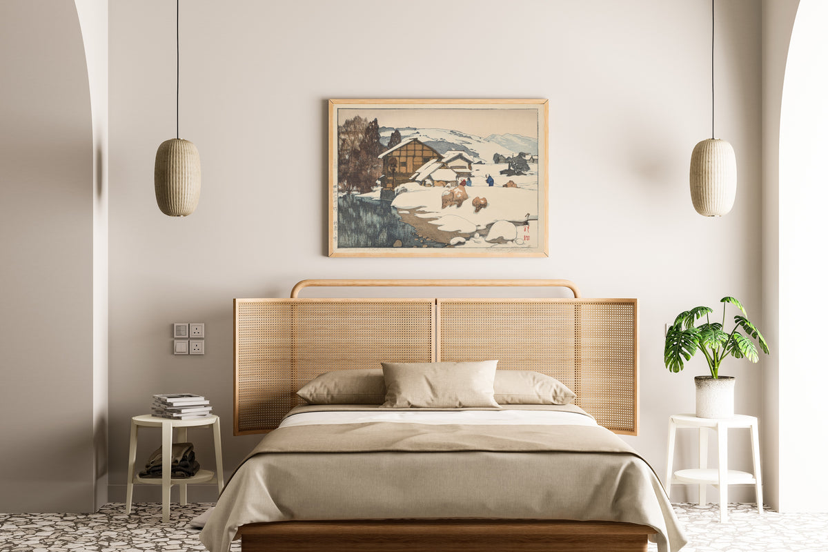 Framed art print of Snow at Kashiwabara by Hiroshi Yoshida, above a cane-headboard bed