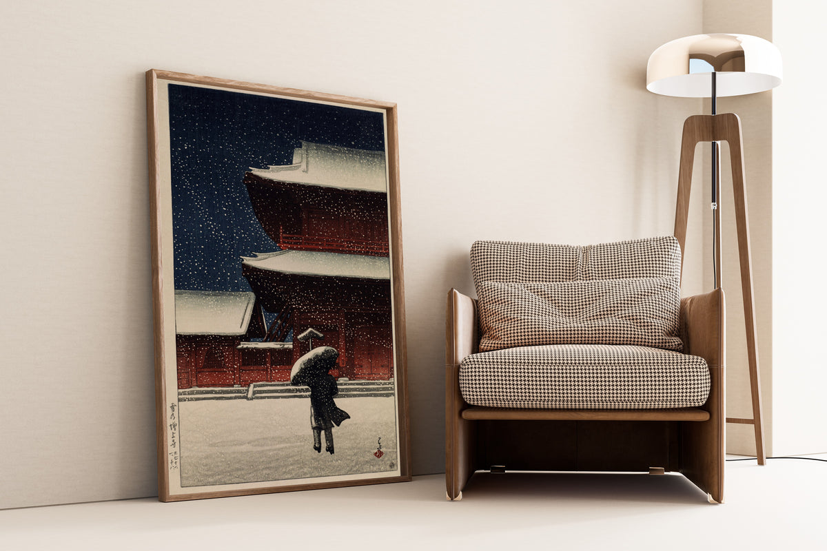 Framed art print of Snow at Zojoji Temple (1922) by Kawase Hasui, leaning against a wall beside an armchair and a floor lamp