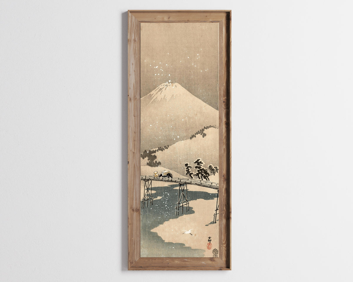 Framed art print of Snowy Landscape with Mount Fuji by Ohara Koson, in a tall wooden frame on a pale wall