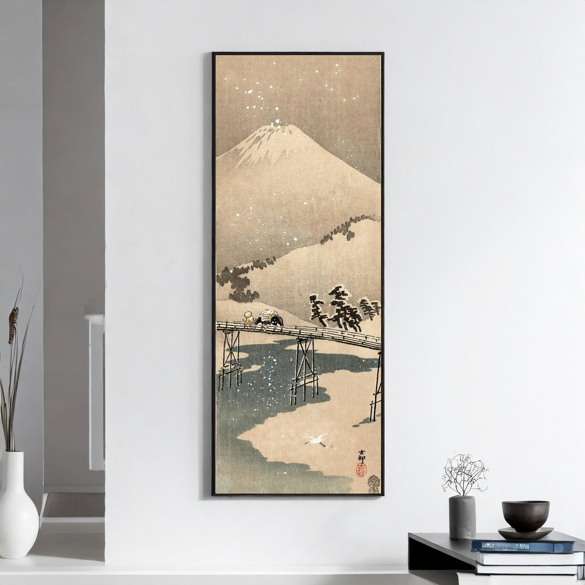 Framed art print of Snowy Landscape with Mount Fuji by Ohara Koson, on a white wall above books and a bowl