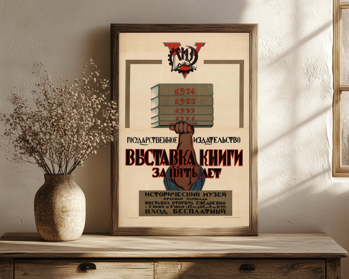 Framed art print of State Publishing House: five years of the book exhibition, in a dark wood frame leaning on a rustic console beside dried flowers