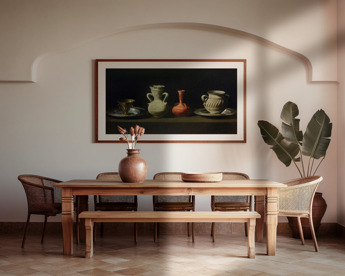 Framed art print of Still Life with Vessels by Francisco de Zurbarán, above a wooden dining table