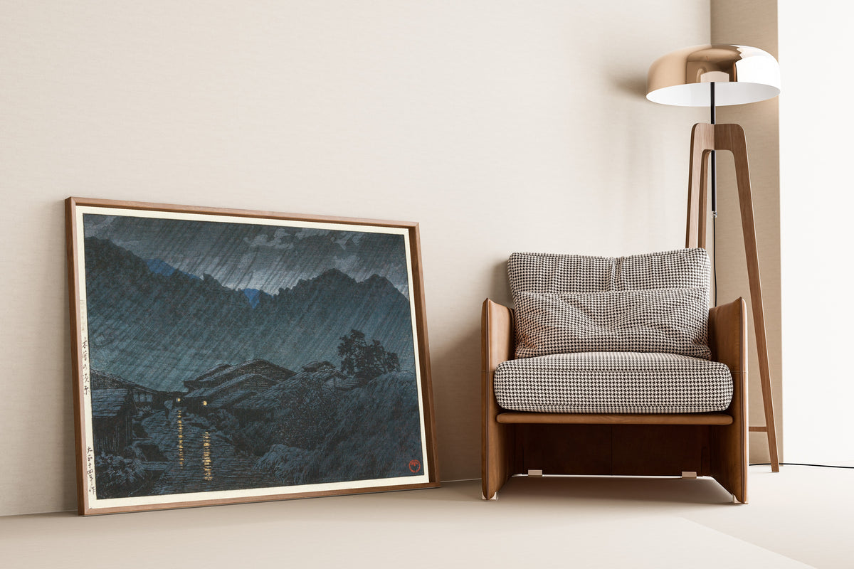 Framed art print of Suhara, Kiso by Kawase Hasui, leaning against a wall beside an armchair and a floor lamp
